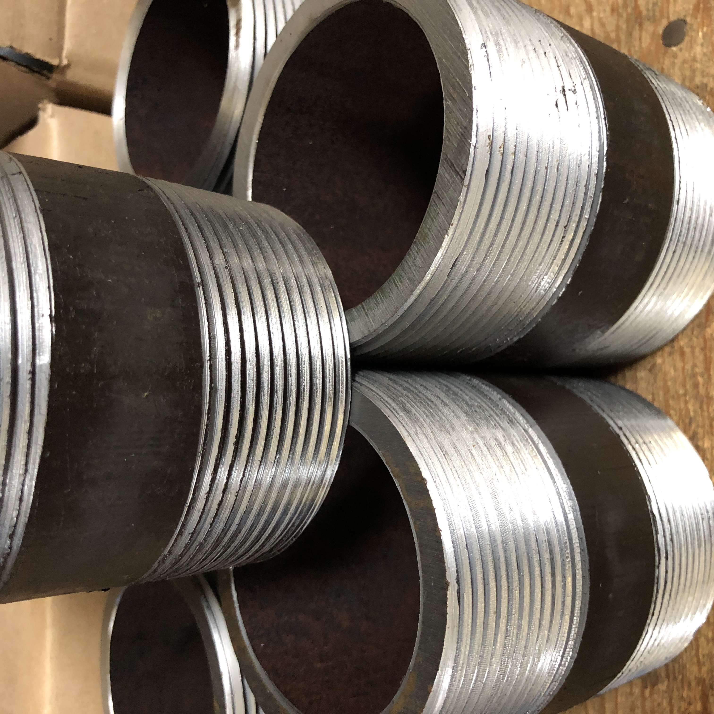 Close-up of large diameter black steel pipe nipples showing precision machined NPT threads